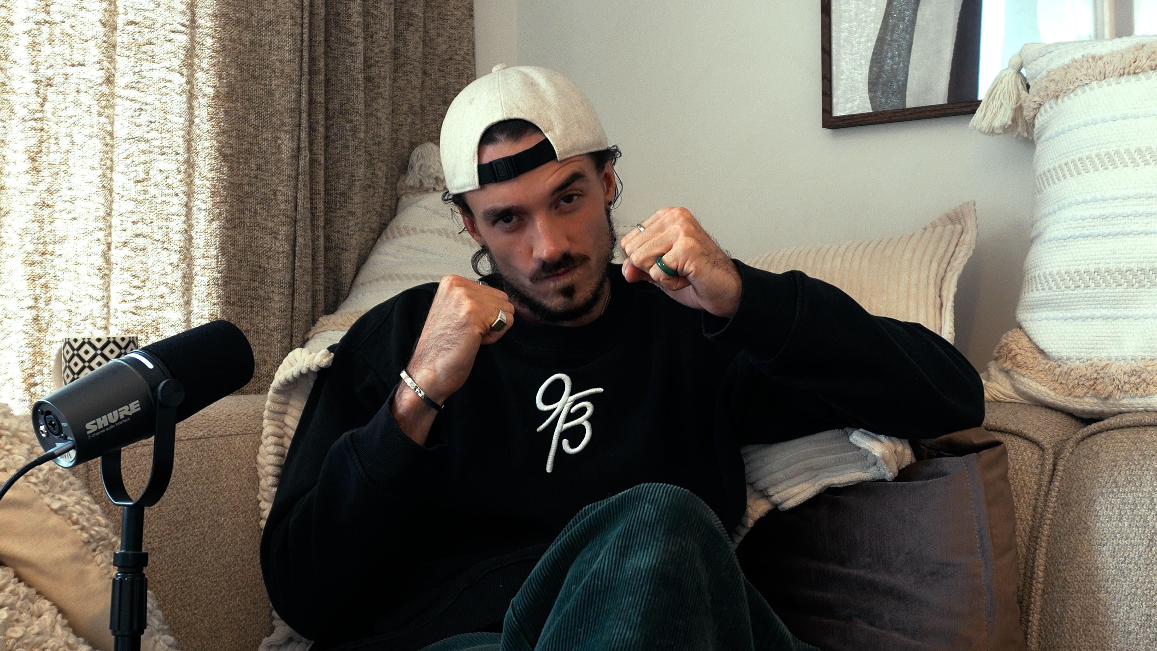Ybelion (Samuel Le Parc) en posture de boxeur, poings levés, sweat floqué de son sigle, devant son micro de podcast