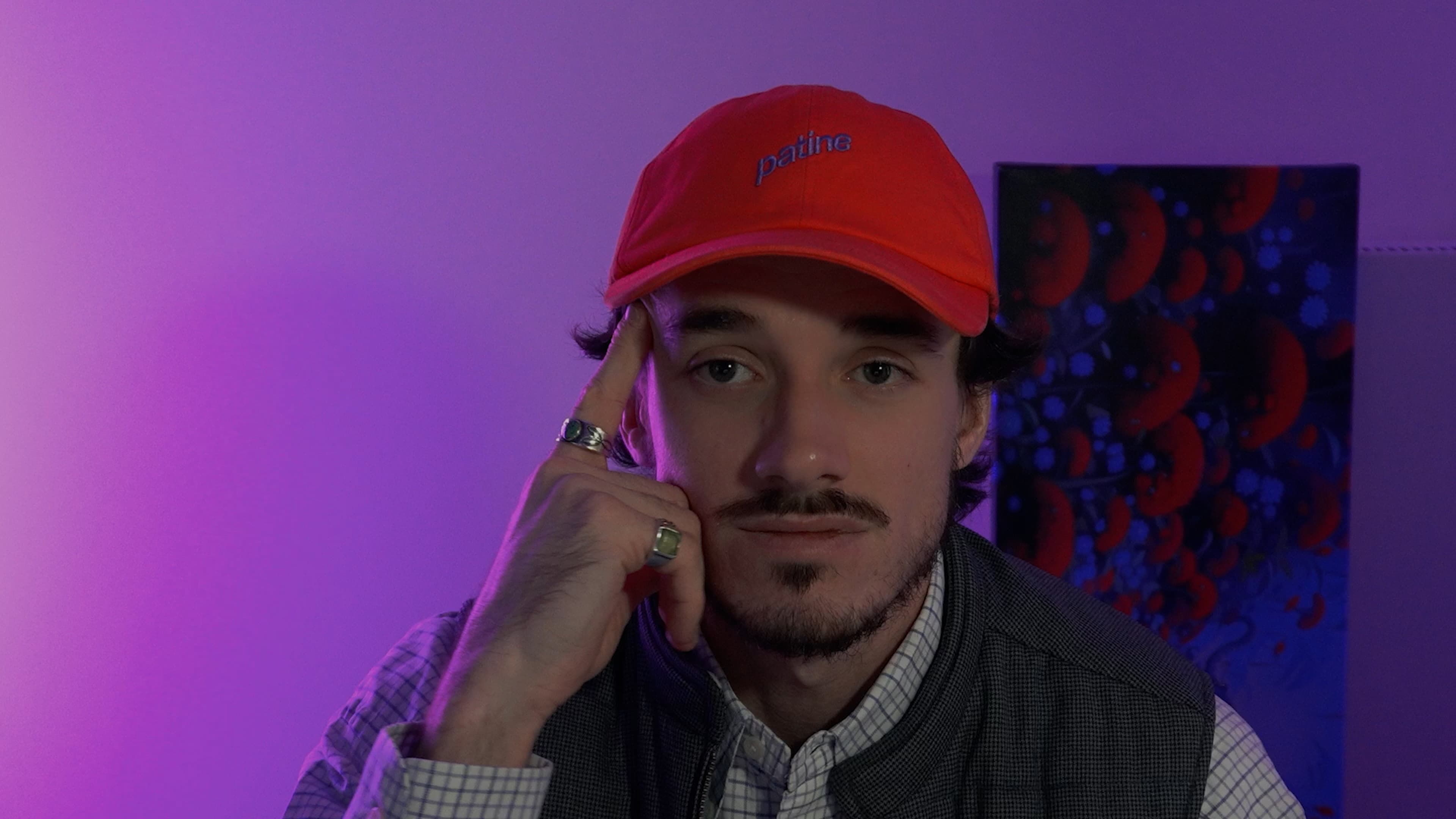 Ybelion (Samuel Le Parc), casquette rouge, main contre la tempe, baigné dans une lumière violette