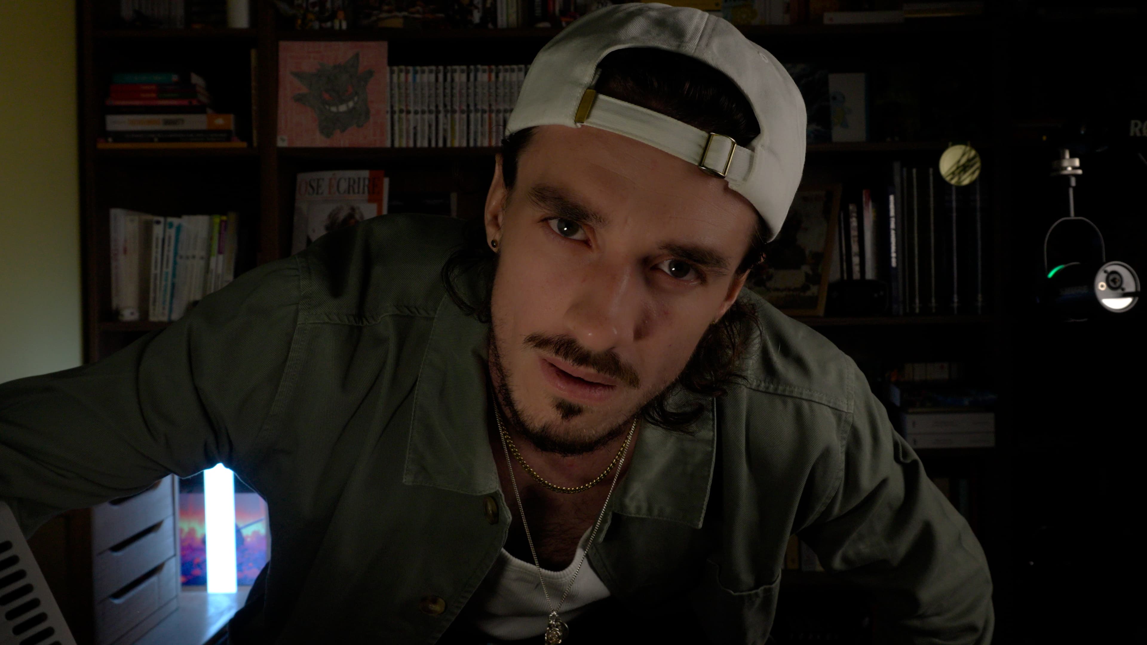 Ybelion (Samuel Le Parc), casquette blanche à l'envers, regard intense face caméra devant une bibliothèque de mangas.