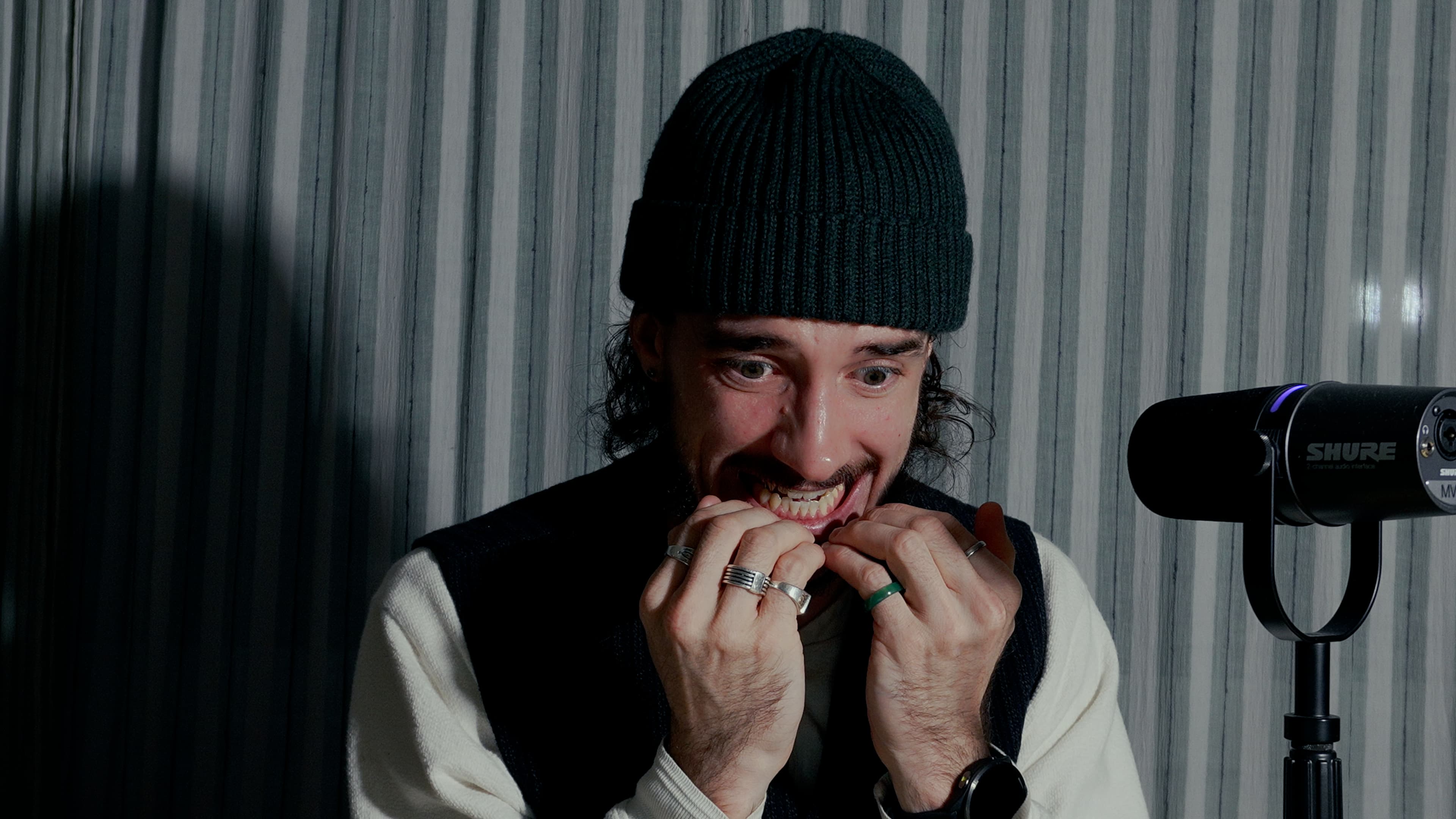 Ybelion (Samuel Le Parc), bonnet noir, se rongeant les ongles avec anxiété devant un micro de podcast